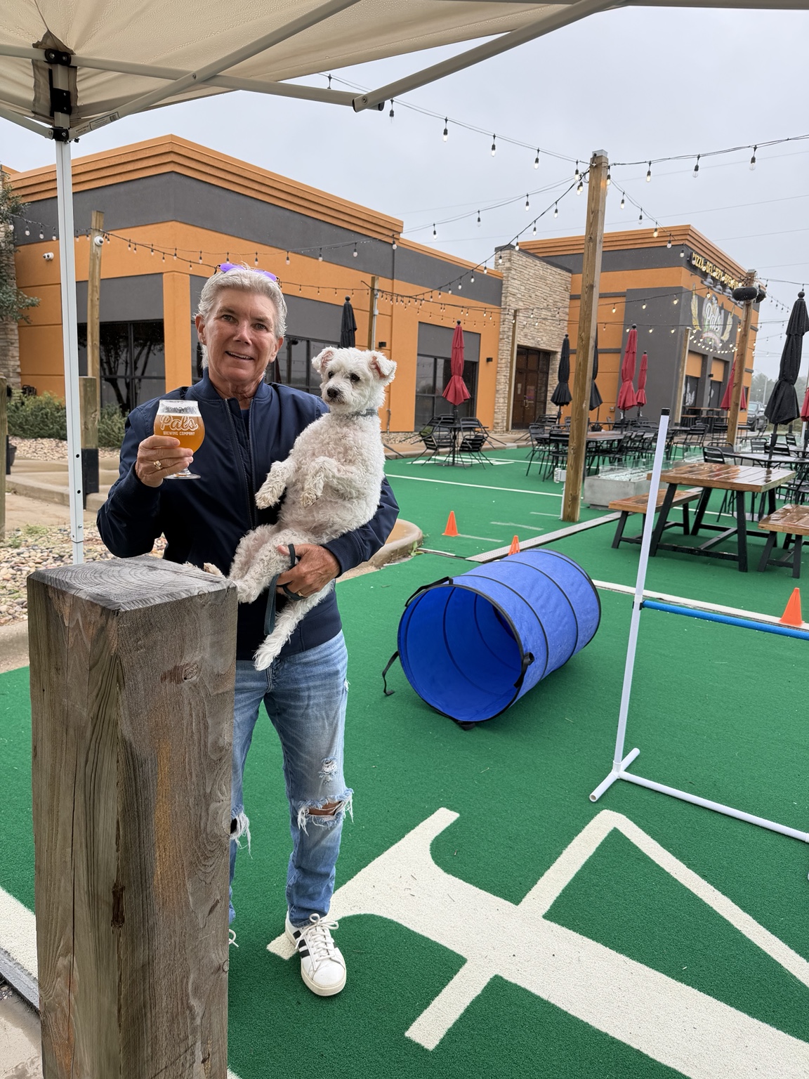 Guest holding her dog and raising a Pals drink beside the course